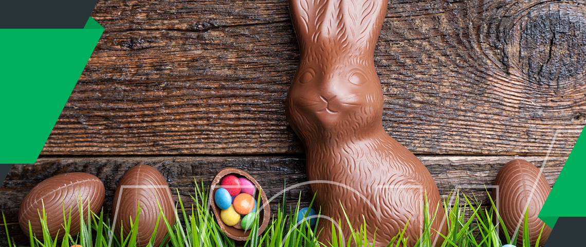 a chocolate easter bunny in front of a wooden board with easter eggs surrounding it.