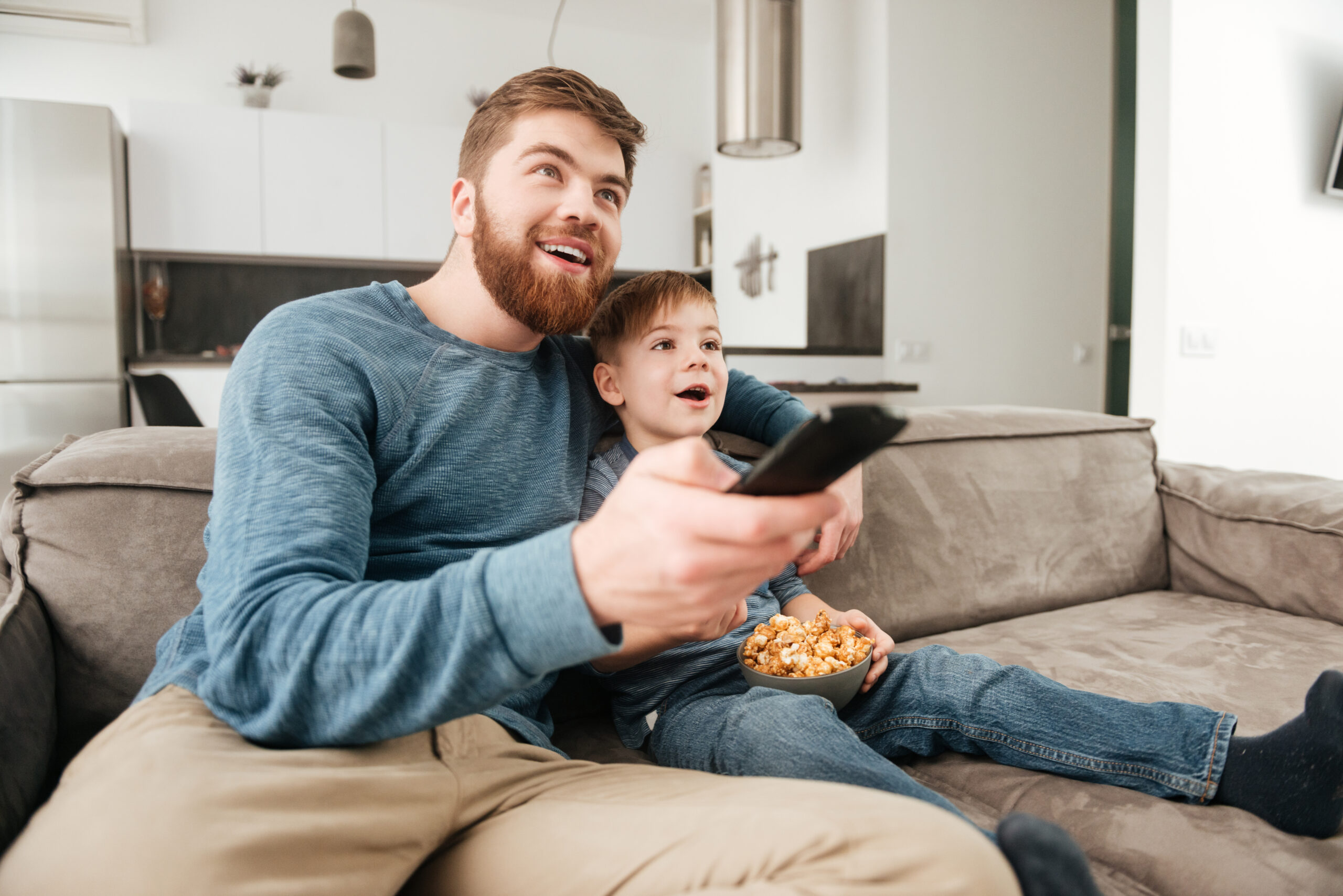 Father and son holding a remote while watching tv