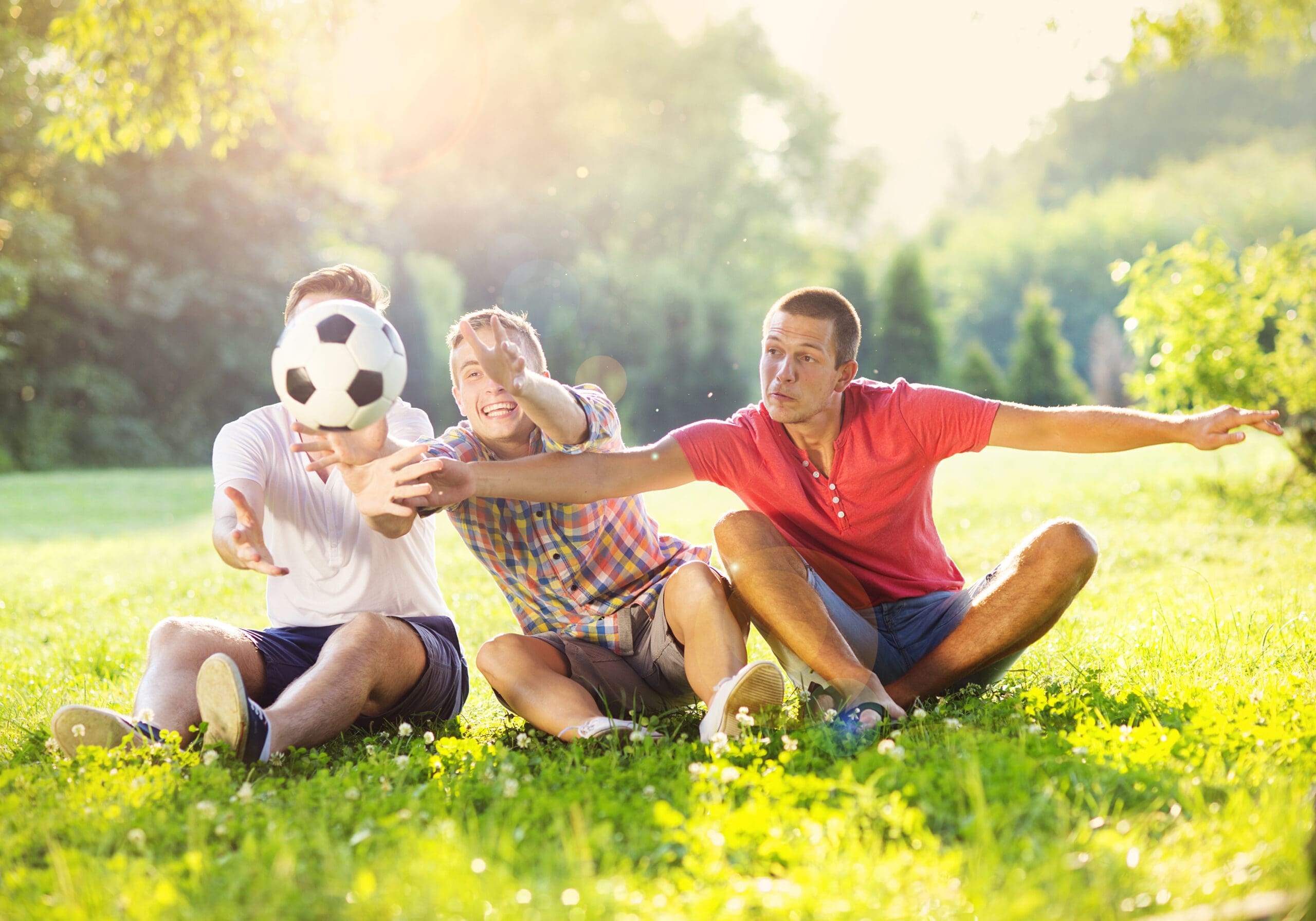 three young men are sitting in the grass playing with a soccer ball in a park